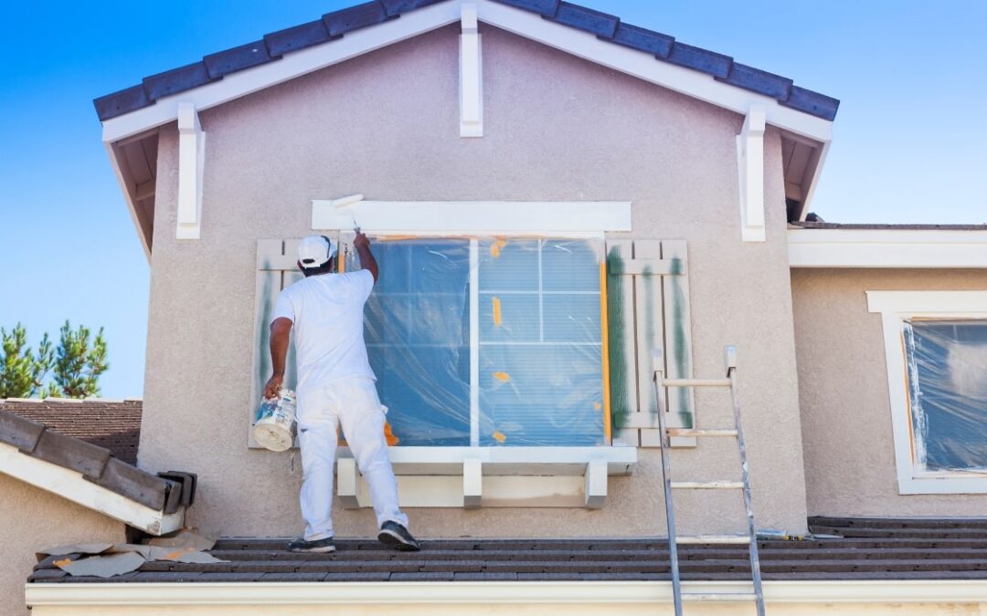 Professional Painter standing on roof painting the exterior of a house